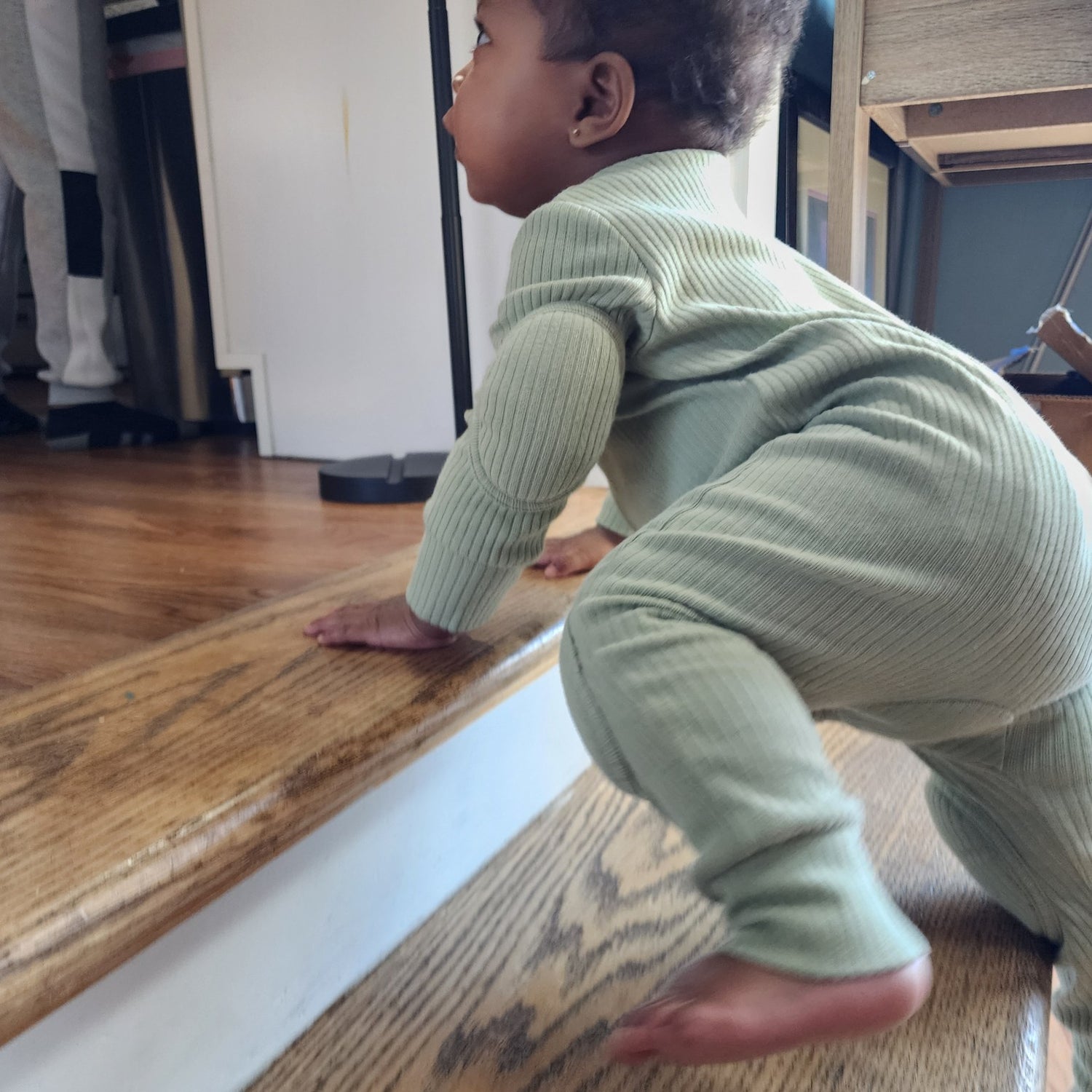 Child climbing stairs in a green NurtureNauts padded romper